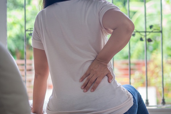 Young woman feeling pain in her back sitting on the sofa at home. Healthcare and medical concept.