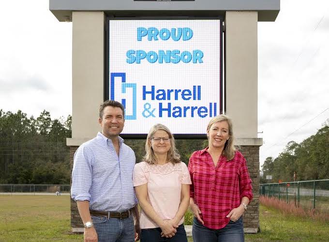 Three adults smile in front of a Harrell & Harrell sign.
