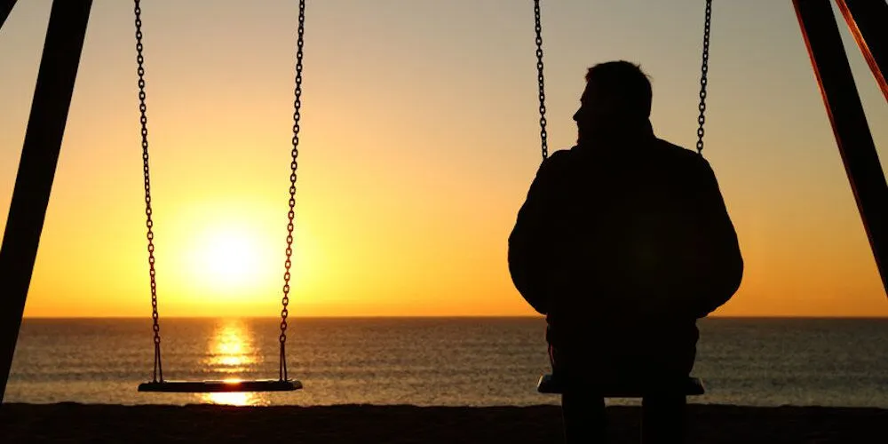 A person sits on a swing facing the ocean.