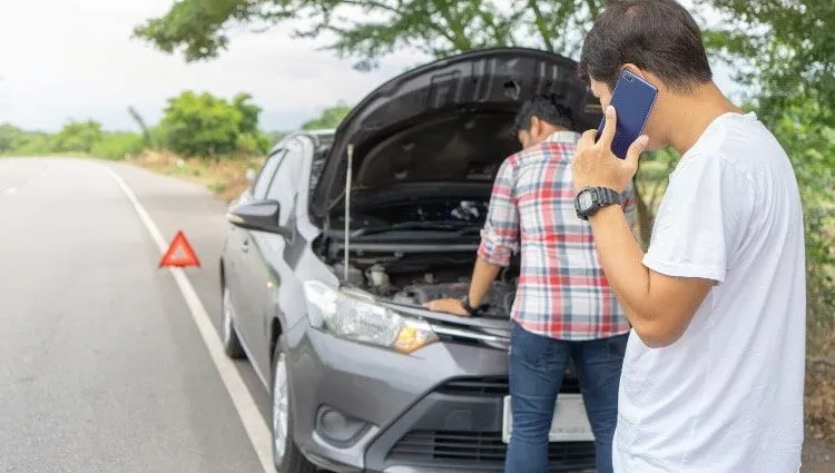 Two men address a car breakdown on the roadside.