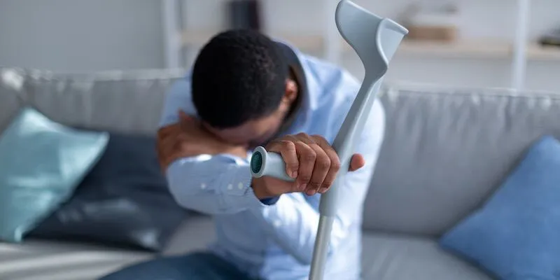 Person on couch holding a crutch and clutching shoulder.