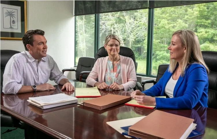 Three people discuss around a table in an office.