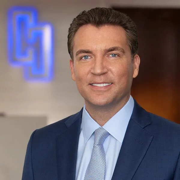 Man in blue suit and patterned tie smiling.