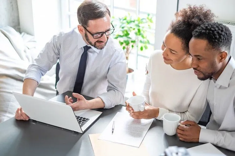 Three people sit at a table looking at a laptop.