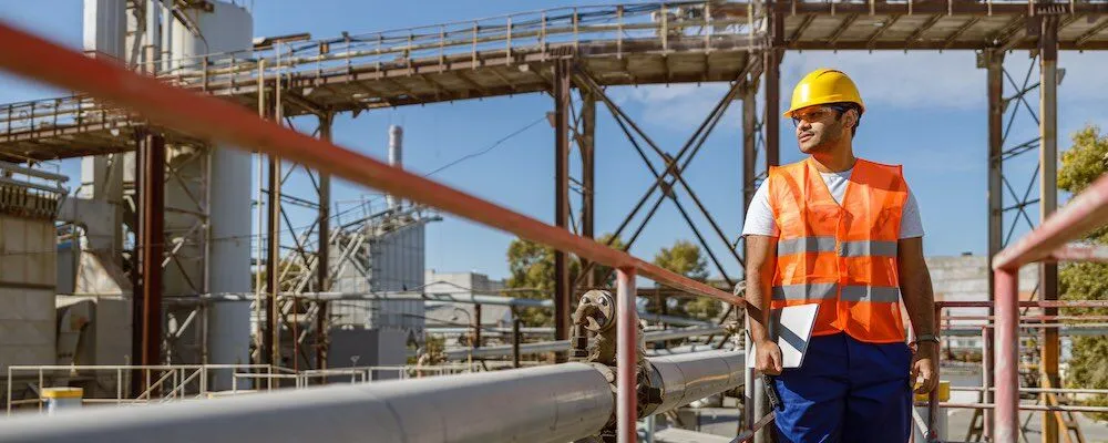 Worker in safety gear holds tablet and looks aside.