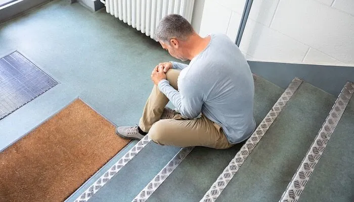 Man sits on stairs holding his knee in pain.