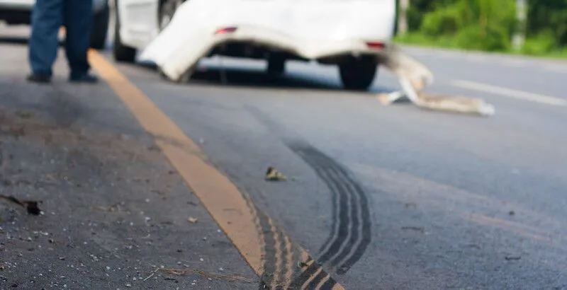 Skid marks on road near damaged white vehicle and person.