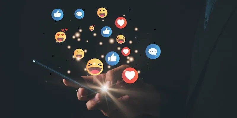 Hand holding smartphone with floating social media reaction icons.