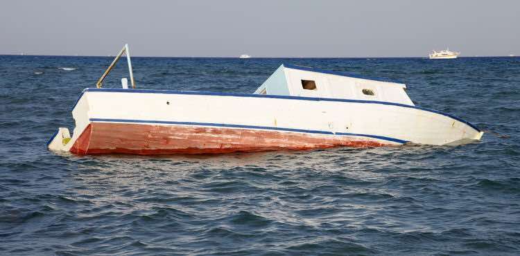 A white and red boat tilts, partially sunken in the ocean.