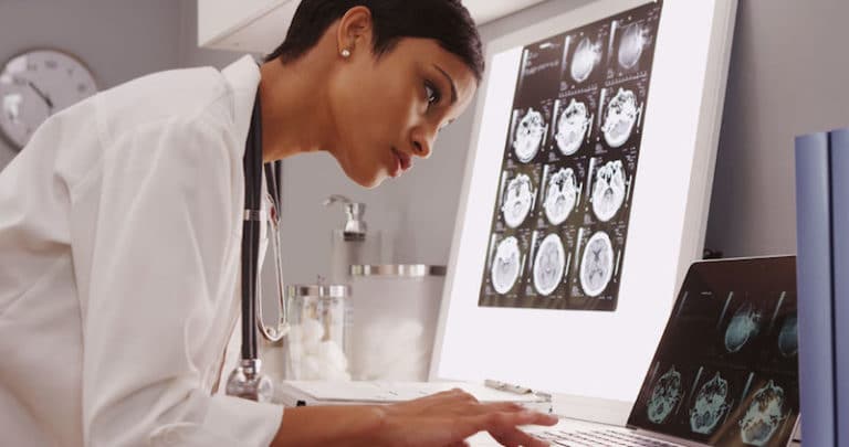 Doctor examines brain scans while typing on laptop.