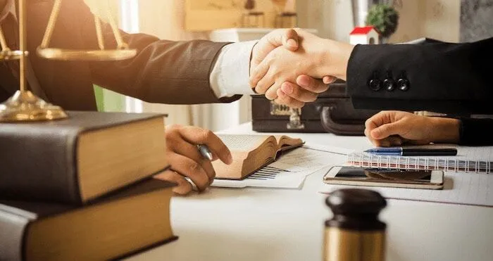 Two people in business attire shake hands across a desk.