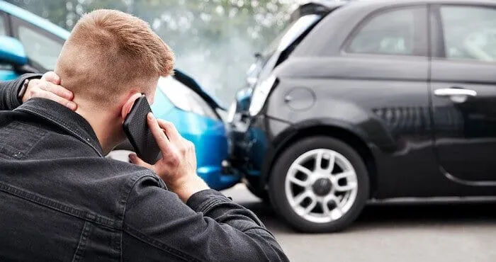 Man holding his neck, talking on phone by crashed cars.