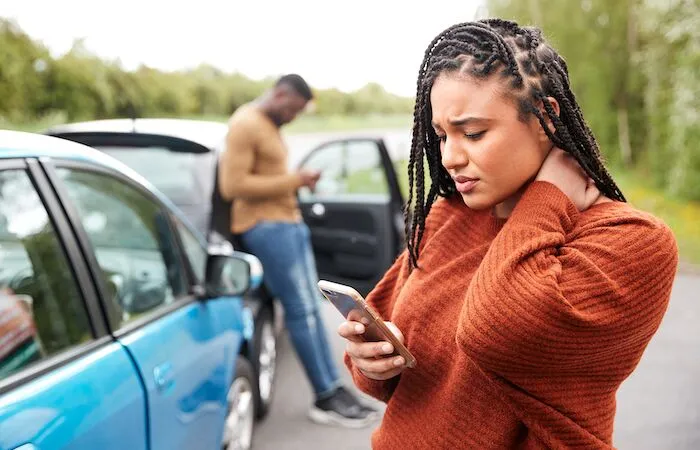 Woman and man use phones beside blue car.