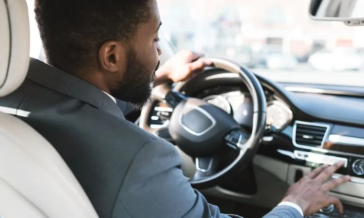 Man in suit drives and adjusts dashboard controls.