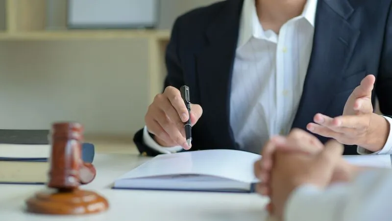 Person in suit gestures with pen at desk.
