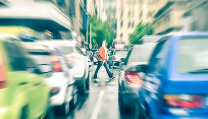 Person in red jacket crosses city street.