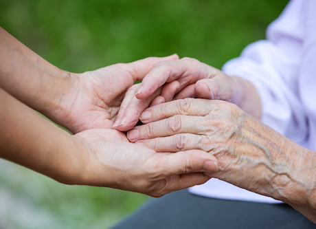 A younger person holding hands with an older person outdoors.