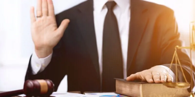 Person in suit raises hand and places other on book.
