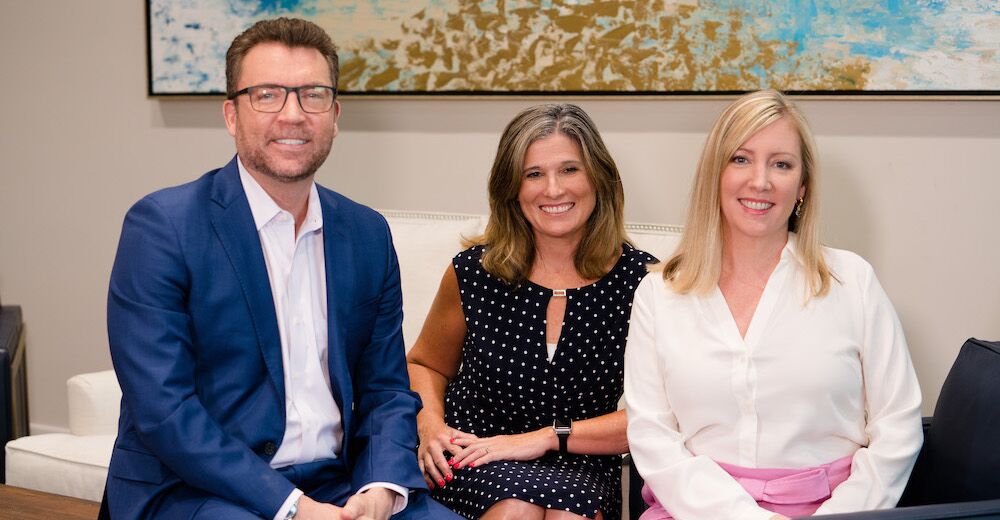 Three people sit on a couch, smiling at the camera.