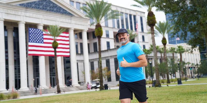 Man jogs on grass while giving a thumbs-up.