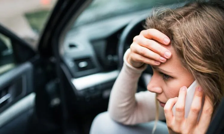 Worried woman sits in car holding phone and her head.