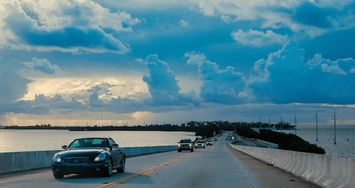 Cars drive across a bridge over water at sunset.