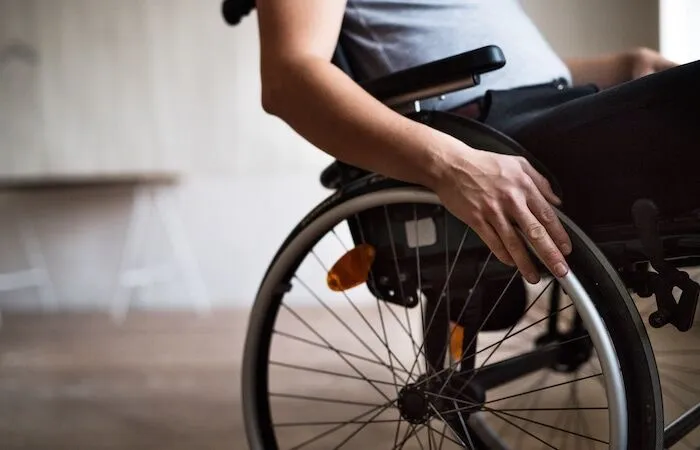 Person’s hand gripping wheelchair wheel indoors.