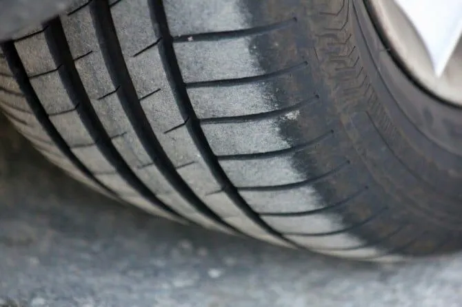 Car tire with uneven tread wear mounted on vehicle.