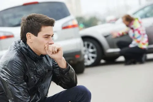 A worried man sits near two crashed cars.