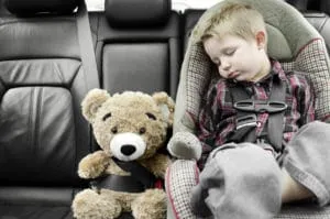 Child sleeps in car seat, teddy bear buckled beside.