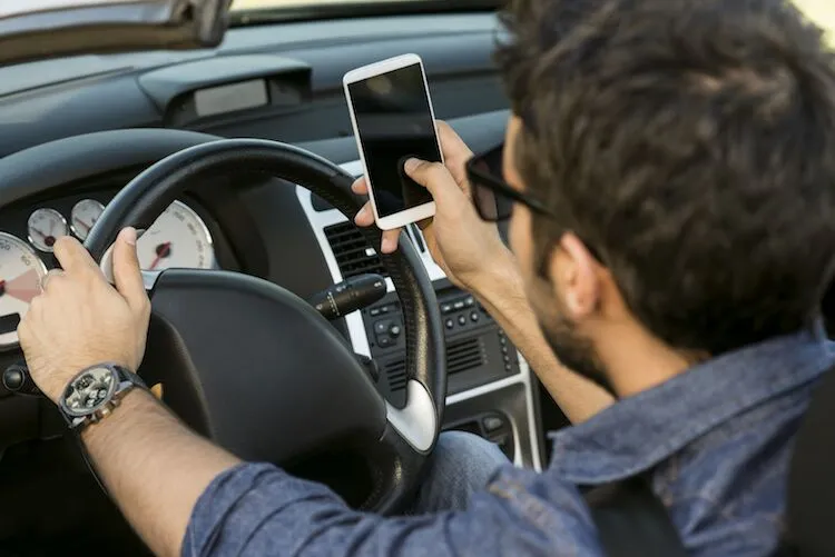 Man drives a car while looking at his smartphone.