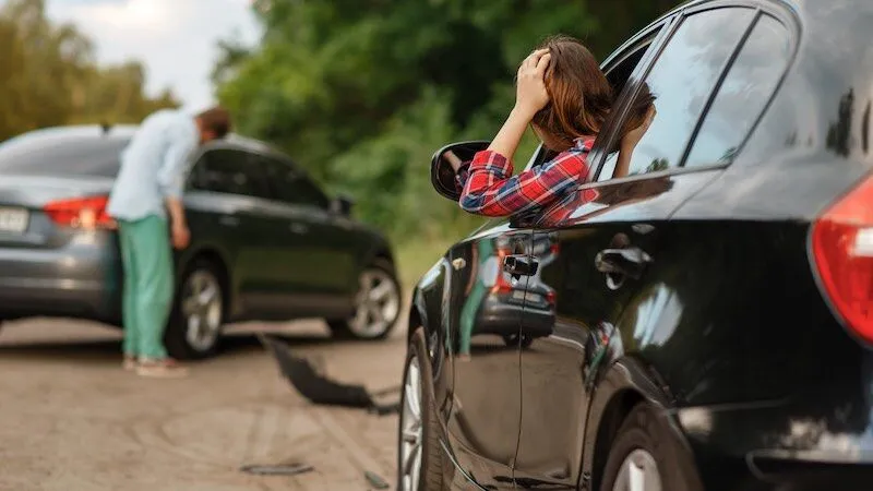Person distressed in black car, another examines gray car.