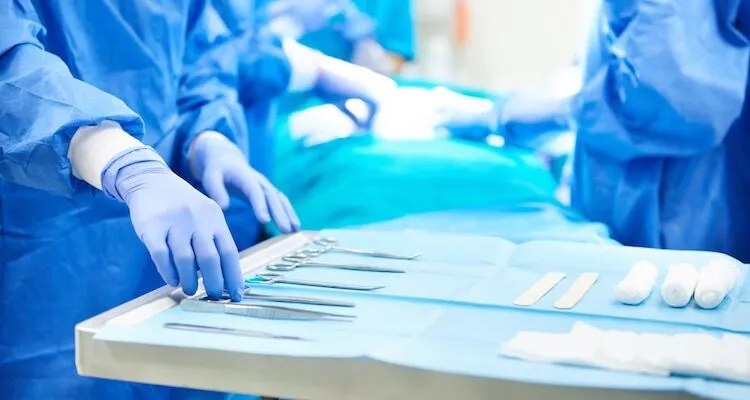 Medical professionals in surgical gowns select tools from a tray.