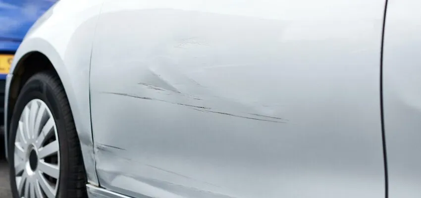 Silver car door with black scratches near rear wheel.