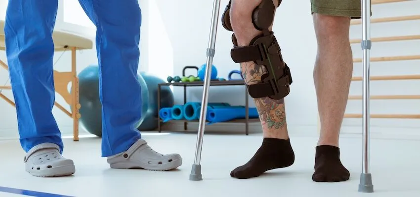 Person with tattoo and knee brace uses crutches.