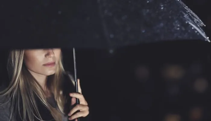 Woman with long blonde hair stands under black umbrella.