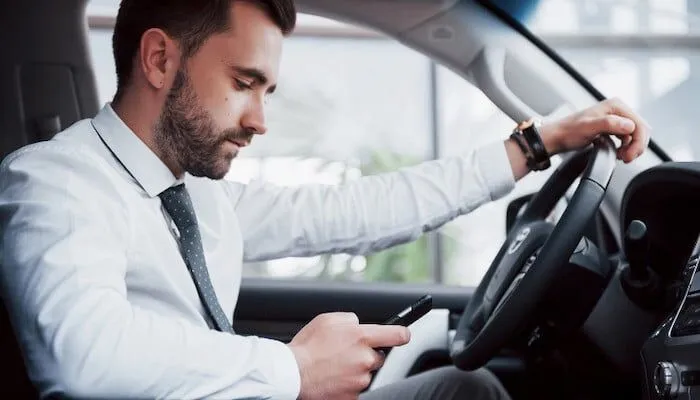 Man in tie sits in car, looking at phone.