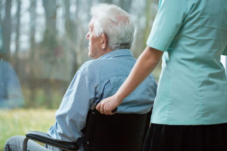 Elderly man in wheelchair looks out window with caregiver.