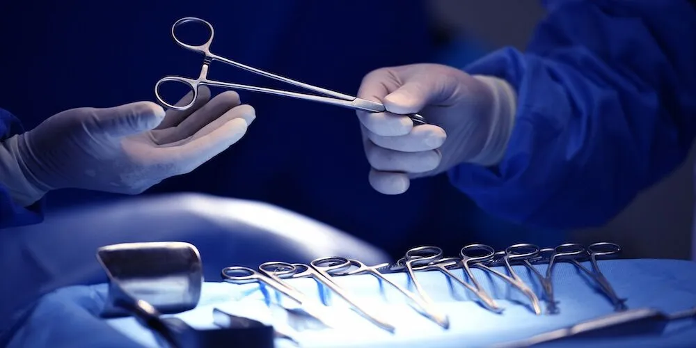 Two surgeons in blue scrubs pass a surgical instrument.
