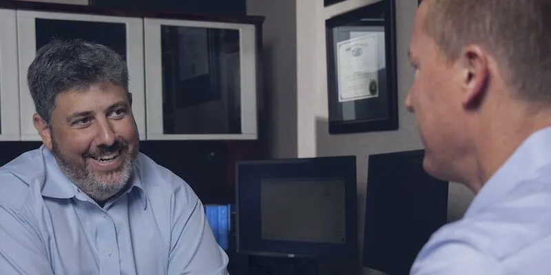 Two men in dress shirts talk in an office.