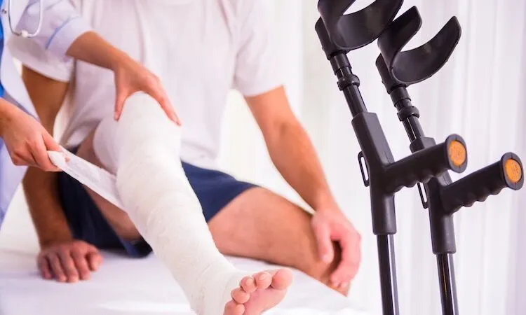 Person with leg cast sits while healthcare worker adjusts bandage.