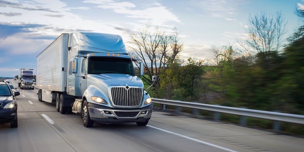 A silver semi-truck drives down the highway.