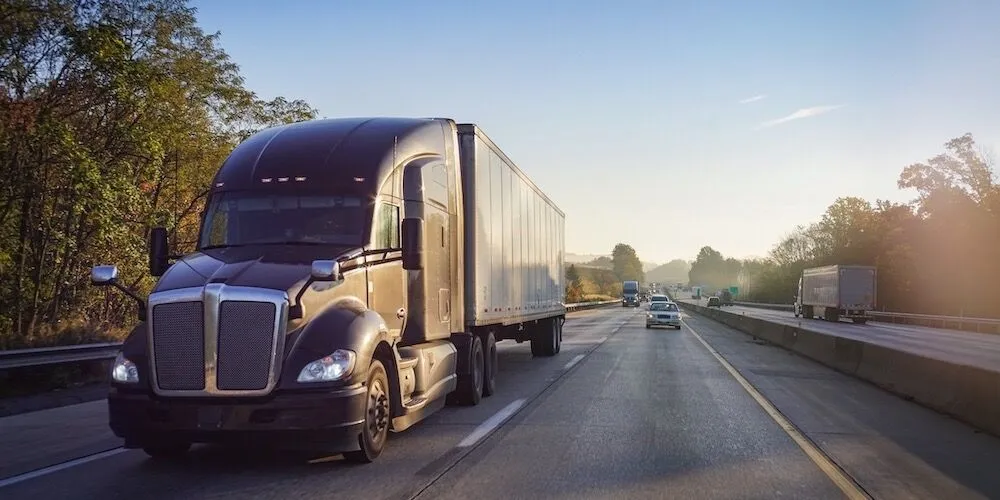 A black semi-truck drives on a tree-lined highway.