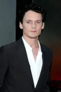 Young man in black suit looks slightly to the side.