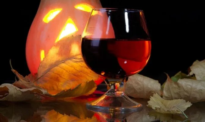 Glass of dark liquor on a table with leaves.