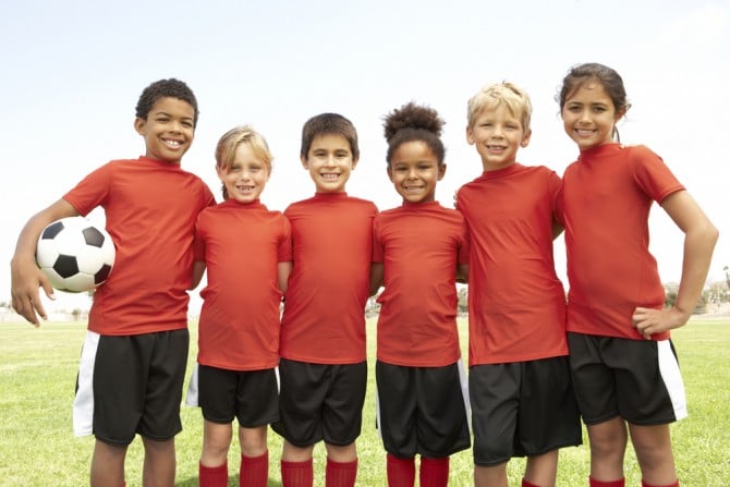 Six children in red soccer uniforms stand smiling together.