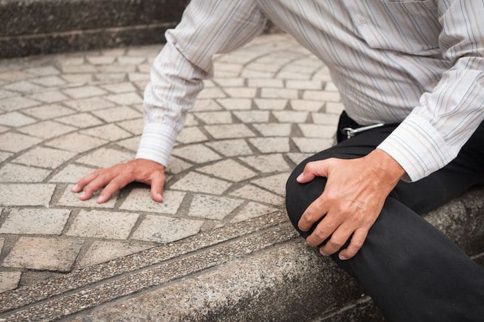 Person in striped shirt sits on stone steps holding knee.