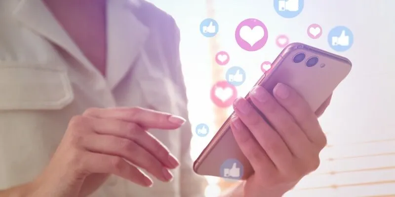 Person using smartphone with social media icons floating above.