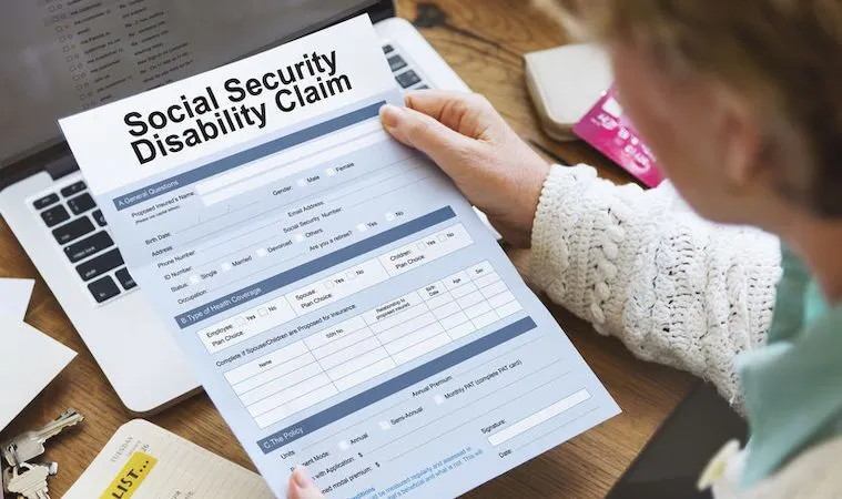 Person holding Social Security Disability Claim form above laptop.