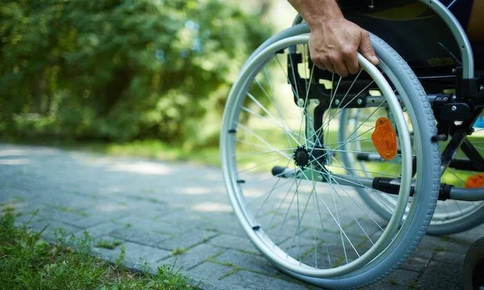 Hand pushing a wheelchair wheel along a path.